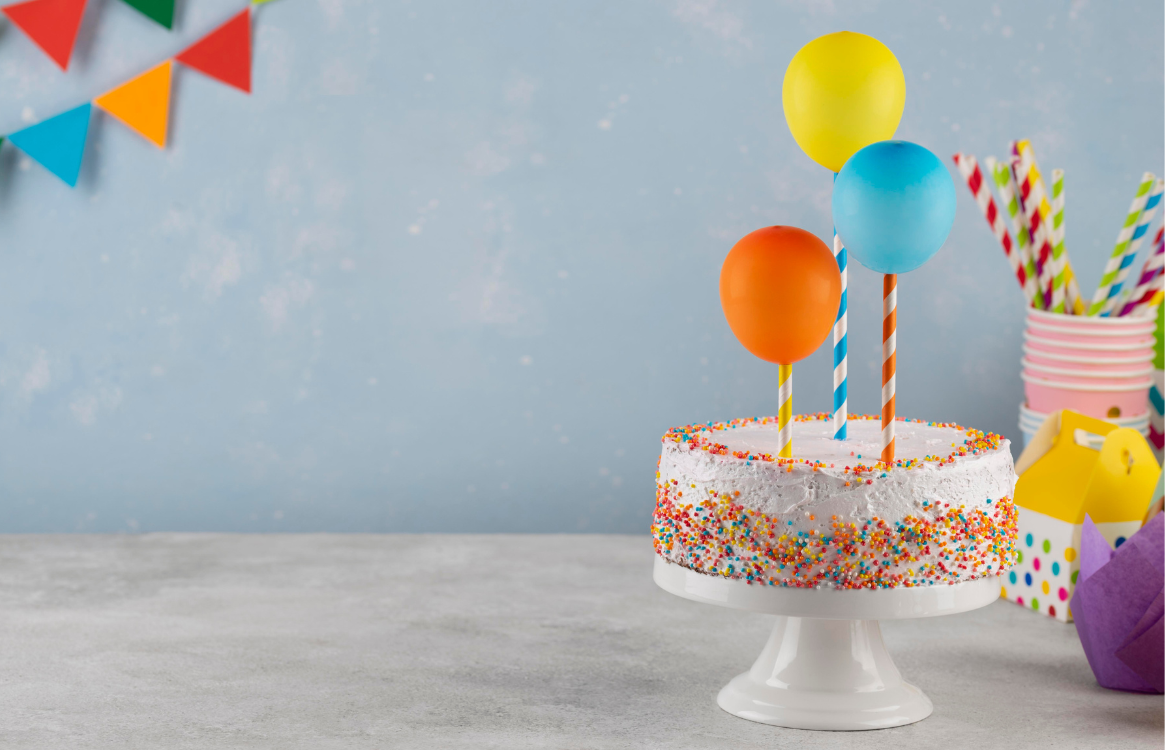 Confetti Birthday Cake on White Table with Blue Background and Party Favors