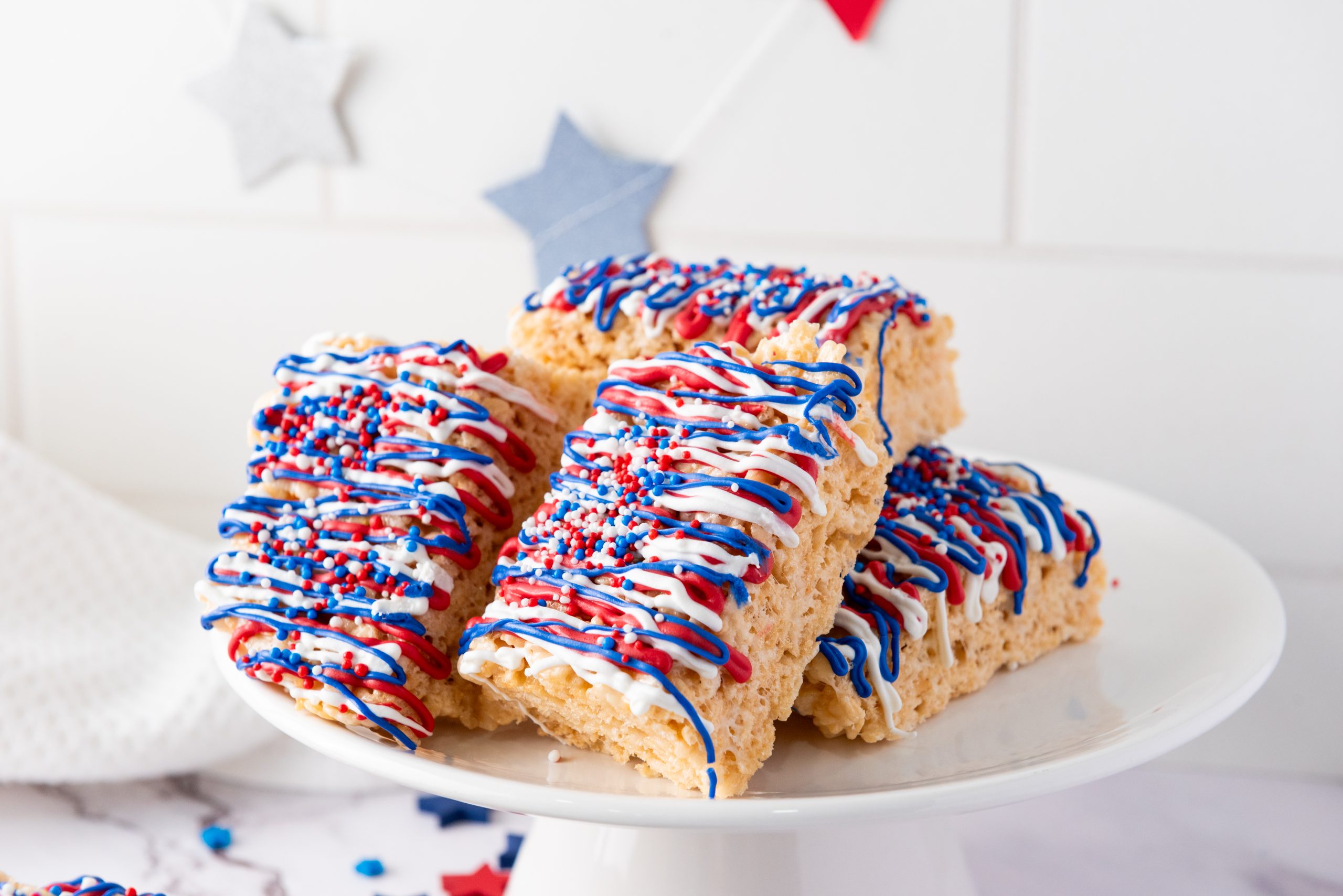 Patriotic themed red, white and blue frosted Rice Krispie treats on white plate.